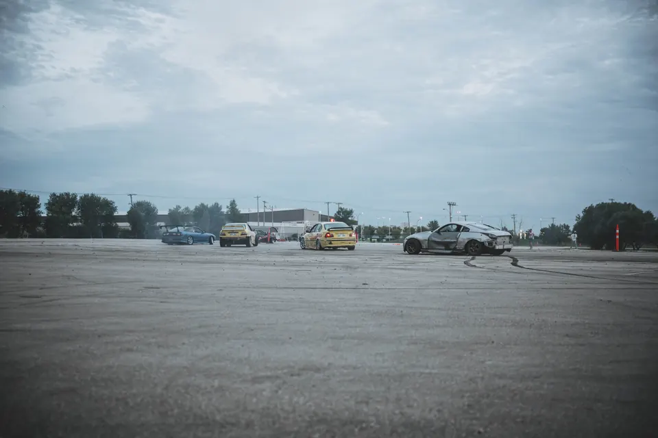 Four drift cars, blue, two yellow, and silver, sliding across a wide concrete lot