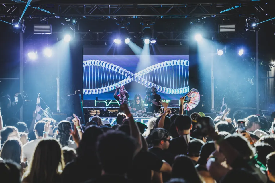 Two people filming from the DJ booth in front of an LED wall, crowd with phones up